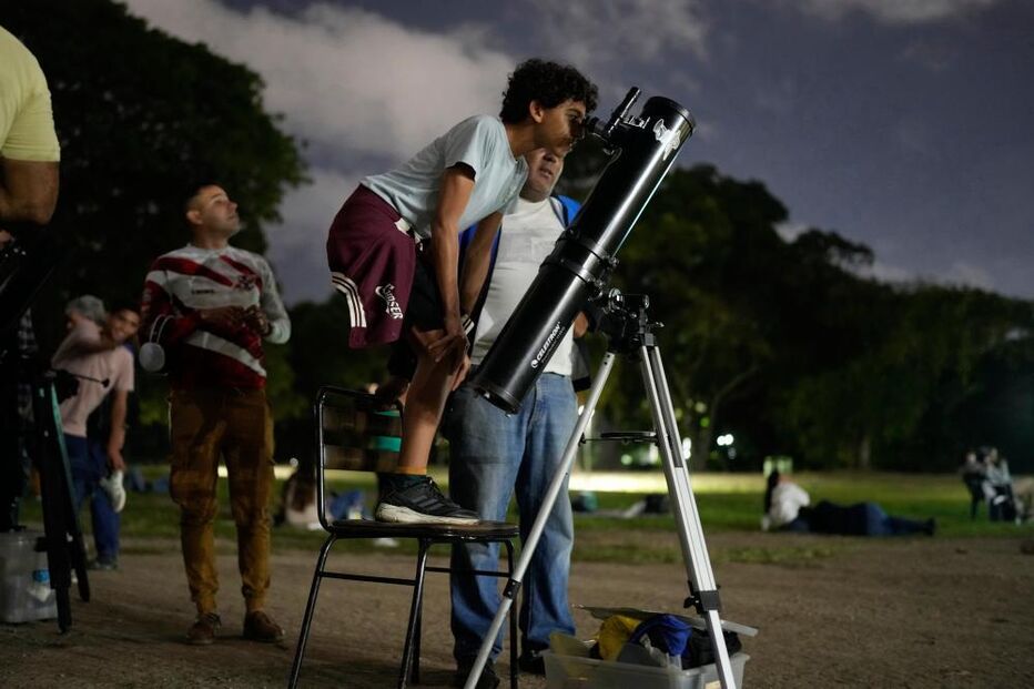 A boy looks at the moon through a telescope during