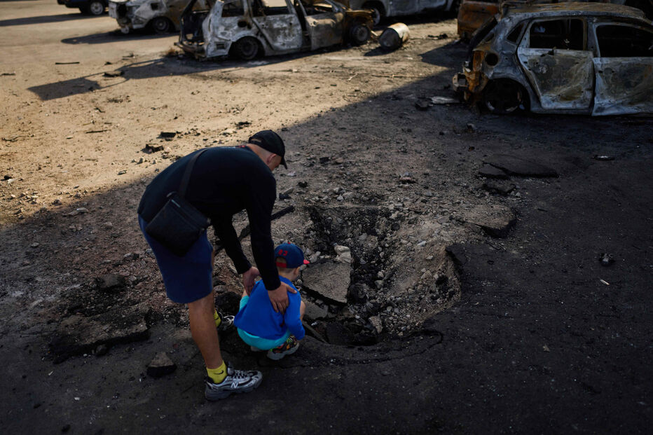 Homem com criança perto de carros destruídos após ataque russo nos arredores de Kiev