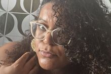 Mulher de óculos com cabelo encaracolado posa para foto com parede gráfica