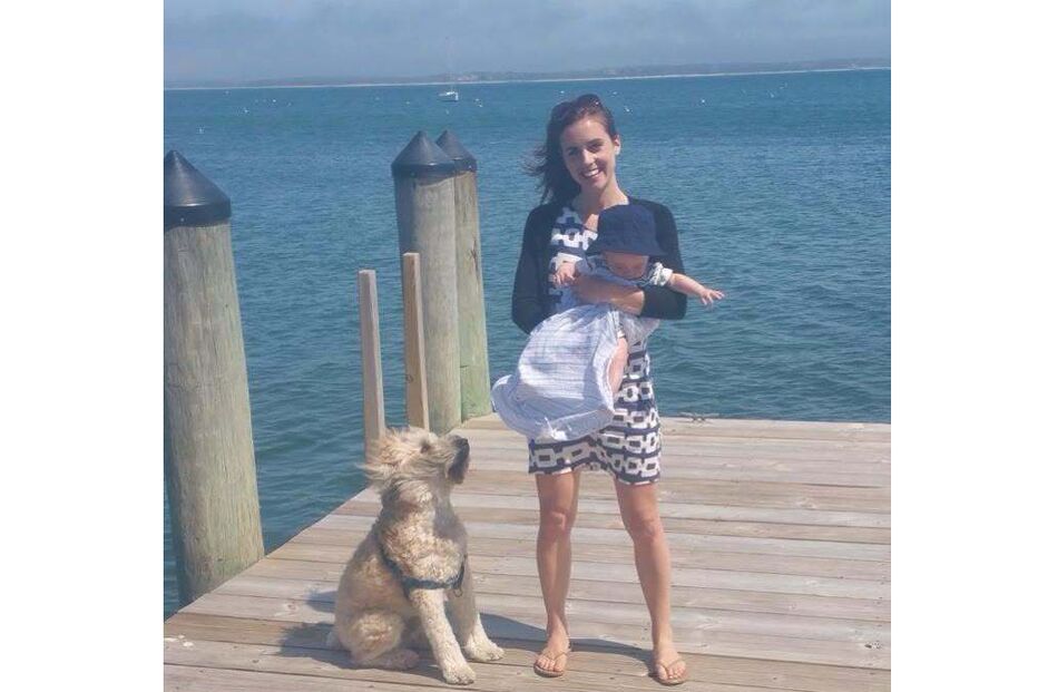 Mulher com bebé e cão num cais junto ao mar