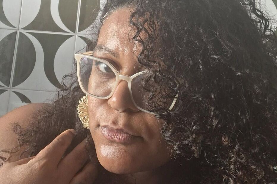 Mulher de óculos com cabelo encaracolado posa para foto com parede gráfica